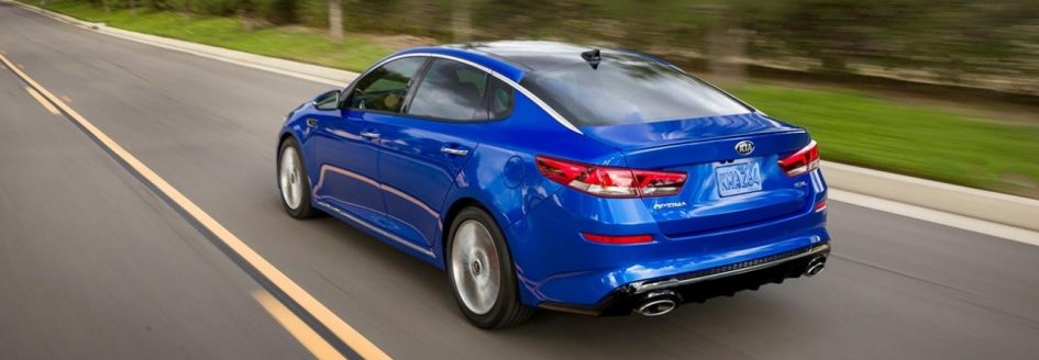 Blue 2019 Kia Optima driving down a country highway.